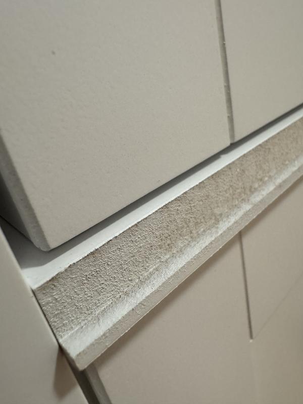 Exposed particle board edge on shelf panel – unfinished, rough, and sharp.