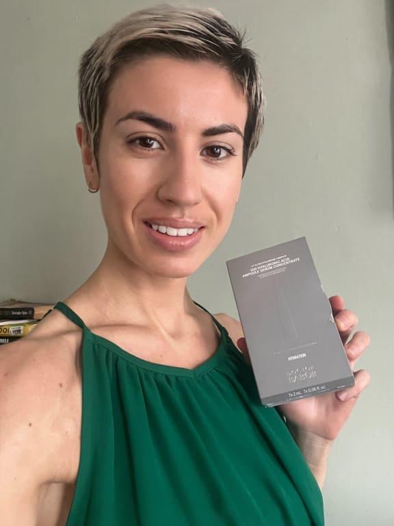Women with short blonde haircut, who is wearing a green top and holding a grey box of 10D Hyaluronic Acid Ampoule Serum Concentrate product