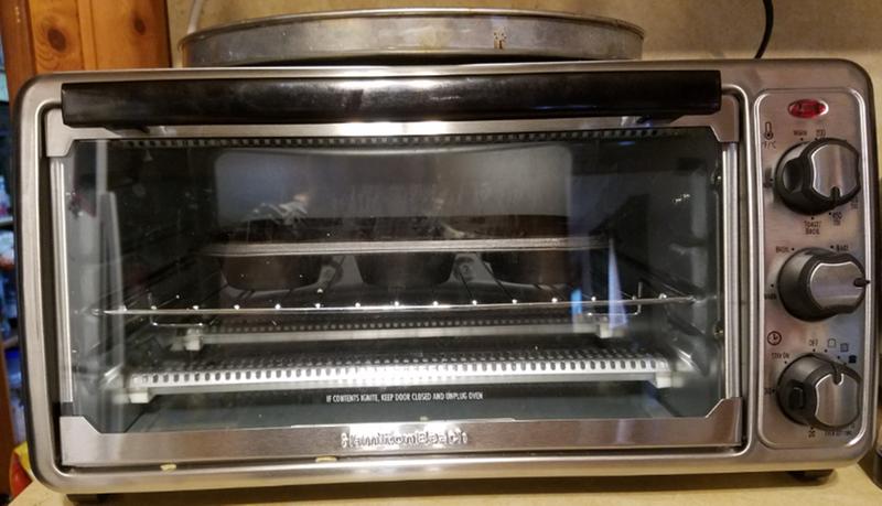 Hamilton Beach Toaster Oven on counter with muffin tin inside and pizza pan on top