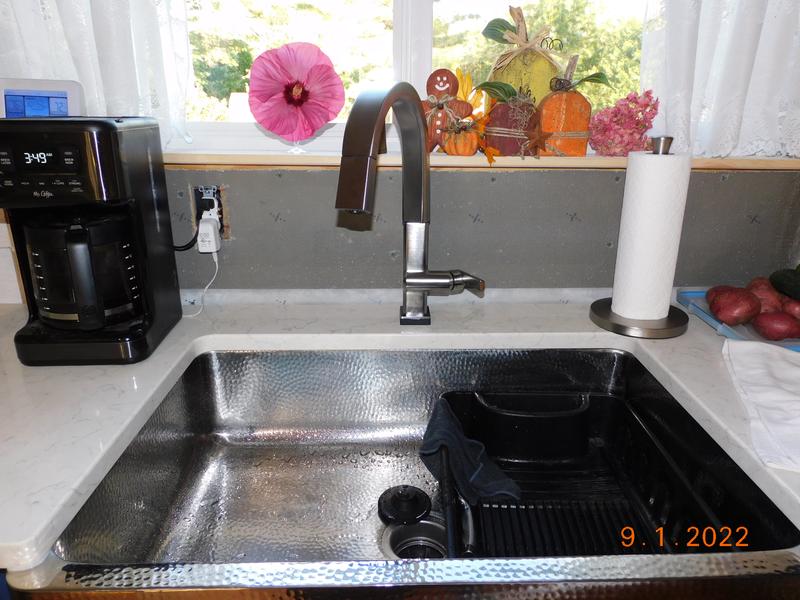 A window is located over a stainless steel apron sink paired with a deck  mount brass faucet and f…