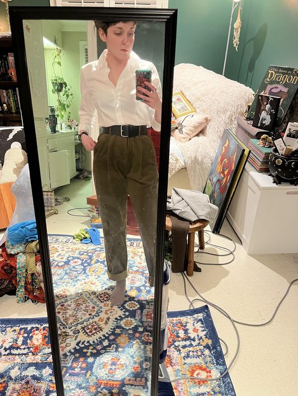 The JNY button up is neatly tucked into olive green corduroy trousers belted with a 2-in black belt with silver rectangle buckle. The v of the top stops just above the top of the bust. a green bra shows very slightly through the white top.
