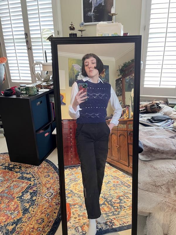 The JNY button up is neatly tucked into black high-waisted jeans. The collar of the button-up folds over a crewneck, knit sweater vest in navy blue. The sleeves of the button-up are cuffed at the wrist. The pits of the top are unobstructed by the vest.