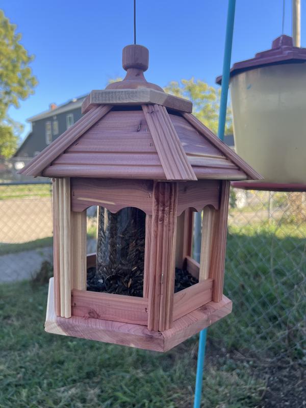 Cedar bird house hanging from a hook.  It is filled with sunflower seeds in the shell