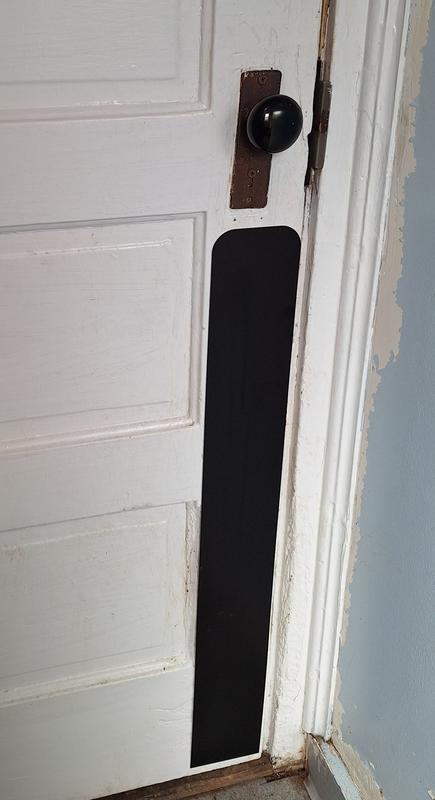 The door plate fits perfectly over the problem area. (Pictured: a white, wooden door with some visible scratch marks on little parts of the door. A matte black, rectangular plate is on the edge and reaches from the doorknob to the bottom of the door.)