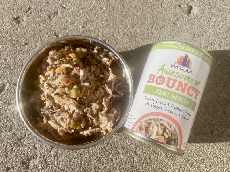 Weruva Awesome Bouncy Joint Health canned wet food pictures in the can as well as a blue bowl.