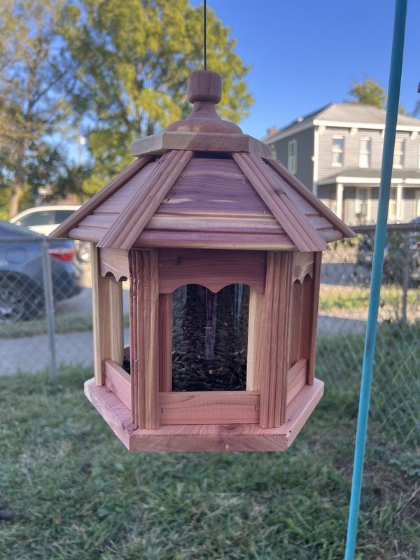 Cedar bird house hanging from a hook.  It is filled with sunflower seeds in the shell