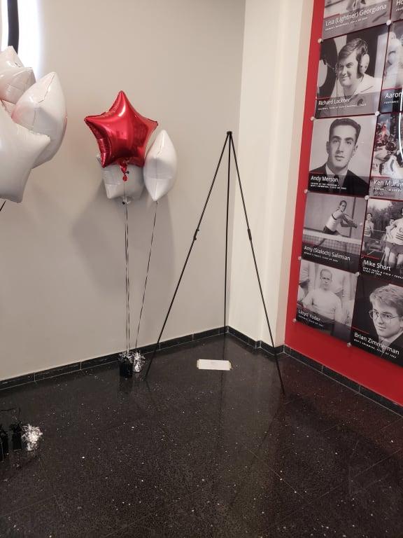 Red and white star balloons being held down by silver and black mini tote balloon weights near an easel that will later hold a poster.